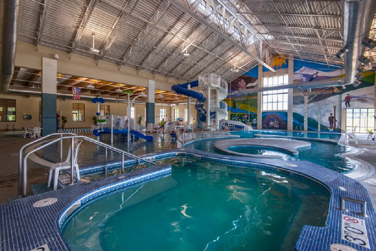 A dynamic indoor recreation center filled with a lively pool area, colorful water slides, playful children, and vibrant murals, all bustling with activity and laughter.