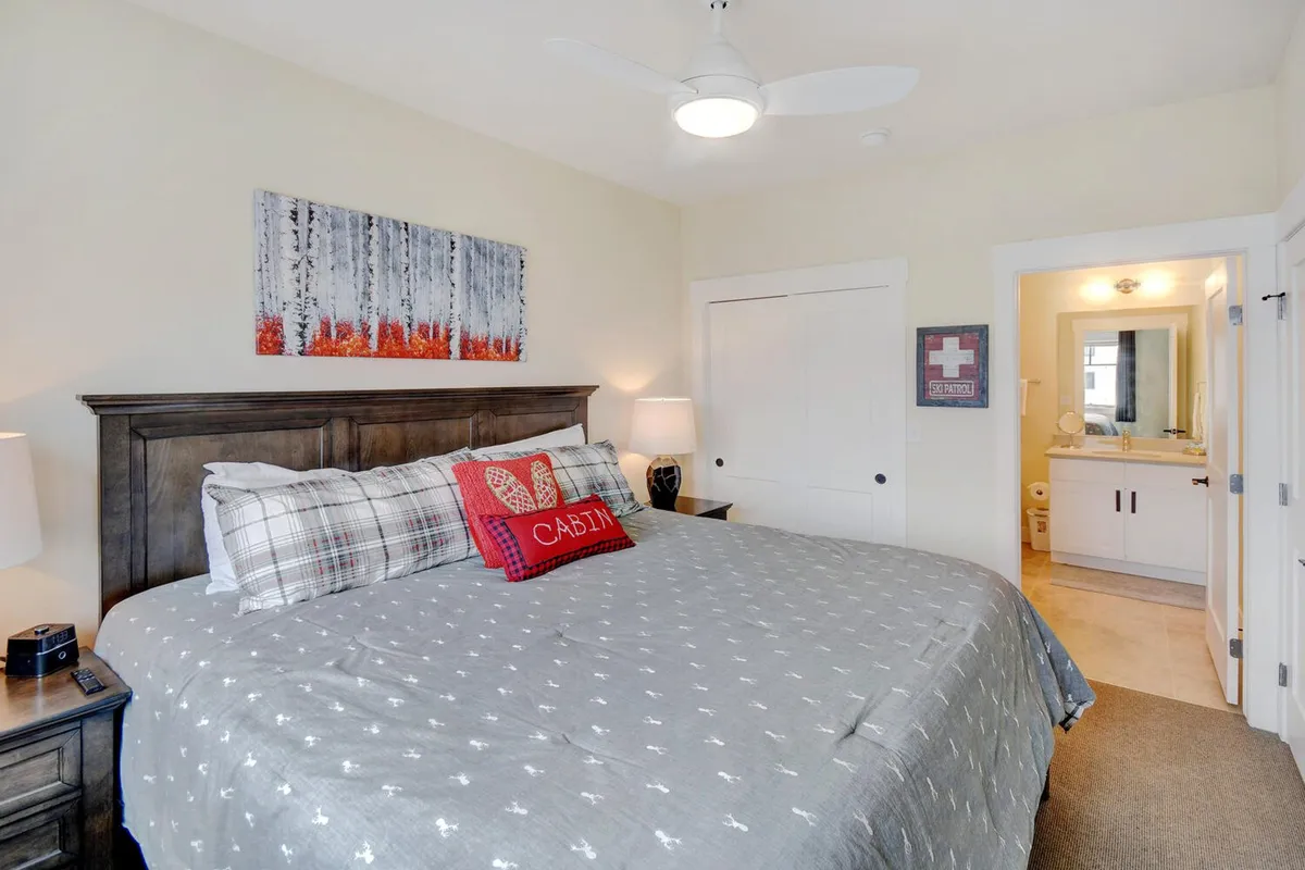 A cozy bedroom featuring a comfortable bed dressed in inviting, premium bedding. Soft blankets, stylish artwork, a nightstand, and a warm lamp create a restful and serene atmosphere bathed in natural morning light.
