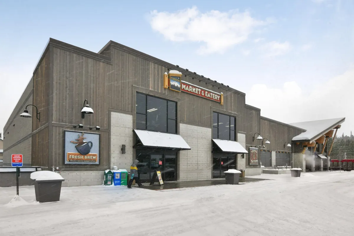 The exterior of the Fireside Market, featuring a welcoming market sign, entrance doors, and a snow-covered outdoor seating area. The scene exudes warmth and local charm, inviting guests to source fresh ingredients and enjoy community events.