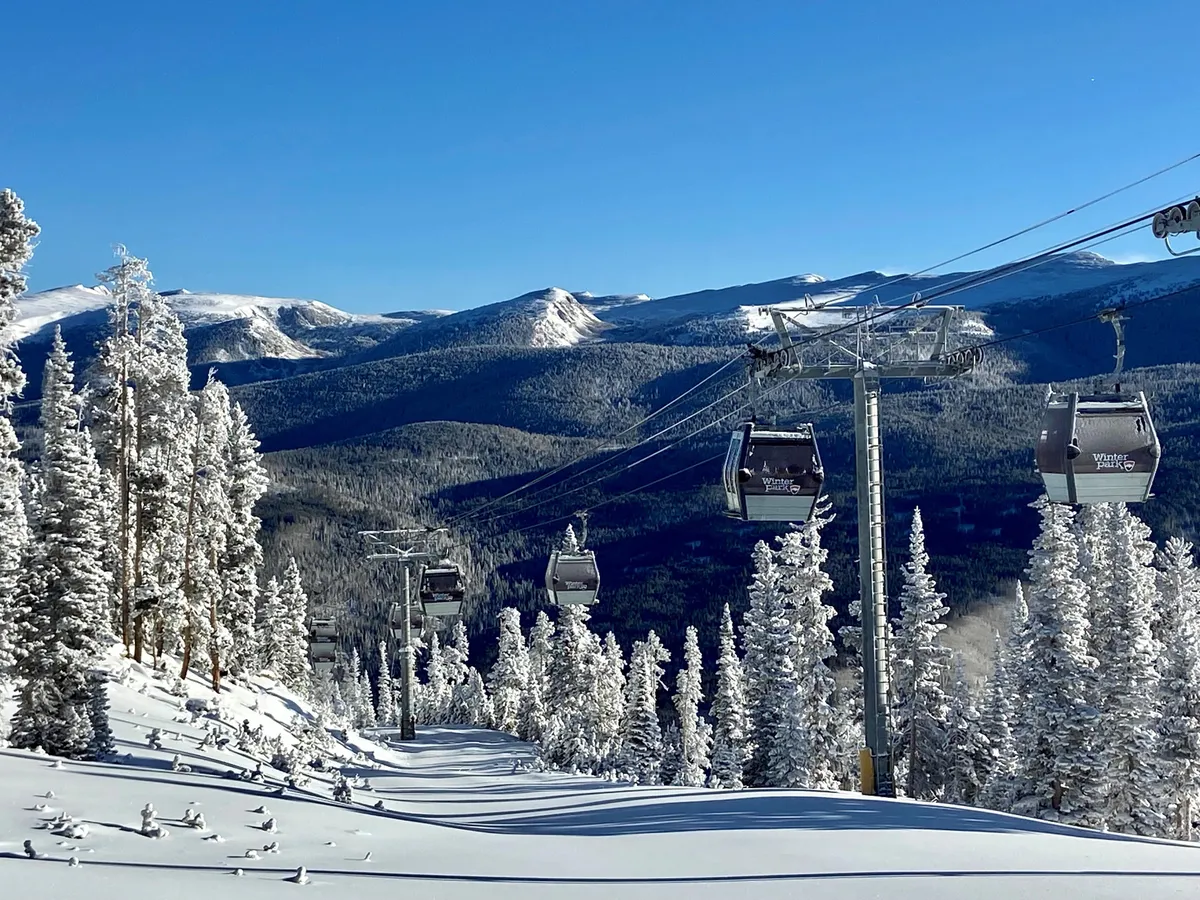 This image captures the exterior of the property with ski lift gondolas, snow-covered trees, and a mountain range stretching across the background. The tranquil winter scene suggests immediate access to outdoor adventures and opportunities to relax with scenic views after a day out.