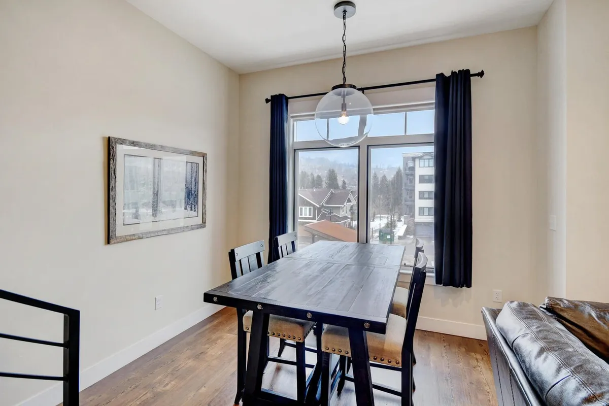 A light-filled dining area with a large dining table set beneath a stylish hanging light fixture. Expansive windows surround the space, providing panoramic views and creating an airy, open atmosphere. The decor is modern yet warm, making it ideal for shared meals, celebrations, or creative work sessions.