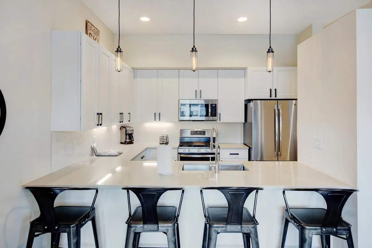 This image captures a modern chef's kitchen with a generous island, elegant pendant lighting, and stainless steel appliances. The layout is designed for both cooking and entertaining, providing ample space for guests to gather, prepare gourmet meals, or simply enjoy a cup of locally roasted coffee.
