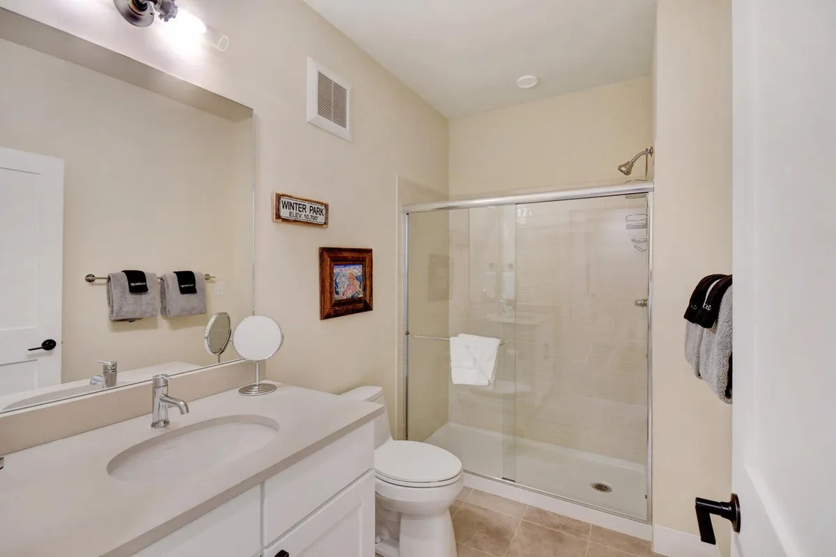 A bright, modern bathroom with a stylish vanity, a spacious glass shower enclosure, fresh towels, and decorative touches. The space exudes a sense of calm and spa-like luxury.